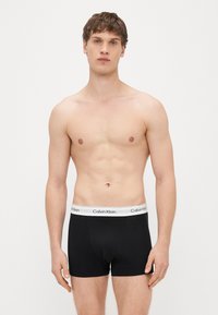 Musta puuvillaiset bokserialushousut, joissa on valkoinen vyötärönauha, jossa "Calvin Klein" -logo, räätälöity istuvuus ja sileä pinta.