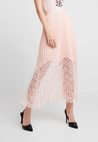 Jupon rose plissé avec un ourlet en dentelle florale, présentant une coupe fluide. Accentué d'une taille lisse et de chaussures à talons hauts noires.