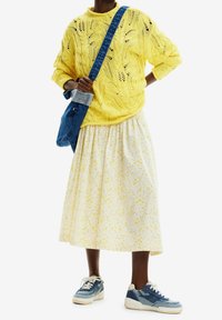 Pull en tricot jaune à coupe ample, jupe blanche à fleurs, et baskets en denim bleu. Comprend un sac épaule en denim.