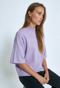 Maglione oversize a maniche corte in lavanda chiaro, realizzato in materiale morbido con un alto colletto a costine e una vestibilità rilassata.