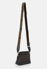 Sort og brun crossbody taske med geometrisk mønster, guldfarvet hardware og en logo-rem. Har en lynlåslukning og en struktureret form.
