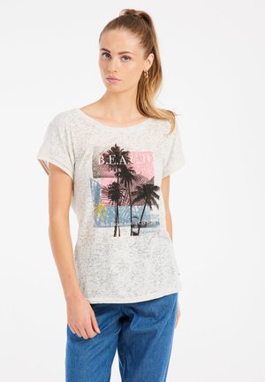 T-shirt gris clair à manches courtes avec graphique de palmier et texte, présentant une coupe ample et un tissu texturé. Assorti à un pantalon en denim bleu.