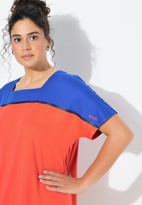 Czerwono-niebieska krótka bluzka z kwadratowym dekoltem i czarnym paskiem dekoracyjnym. Wykonana z gładkiej tkaniny, z logo "sports" na rękawie.