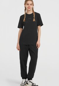 Black cotton t-shirt with short sleeves, rounded neckline, and logo detail. Paired with black jogger pants featuring elastic cuffs and subtle branding.
