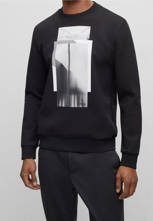 Svart sweatshirt med en framträdande grafisk design med lager av rektangulära former i monokromma toner och vertikala randiga detaljer.