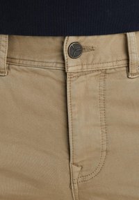 Pantaloni khaki caratterizzati da una texture liscia, design standard a cinque tasche e chiusura con bottone in metallo con branding sul davanti.