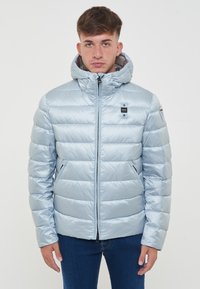 Giacca isolante blu chiaro con finitura lucida, cappuccio, zip frontale e due tasche laterali. Presenta pannelli trapuntati orizzontali.