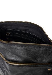 Interno di una borsa in pelle nera con una cerniera dorata. Presenta una tasca con cerniera e una fodera in tessuto semplice. Texture morbida con una forma strutturata.