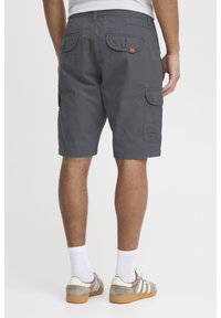 Grijze cargoshorts van een katoenmix, met twee achterzakken met kleppen, zijzakken en een relaxte pasvorm. Draagt met lichtgekleurde sneakers.
