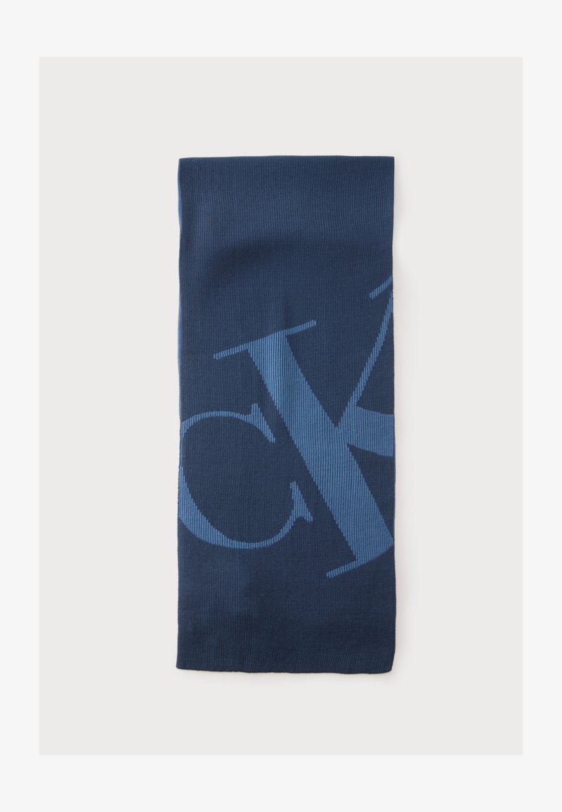 Écharpe tricotée rectangulaire bleu foncé avec de grandes lettres bleu clair partiellement visibles, posée à plat sur un fond blanc.