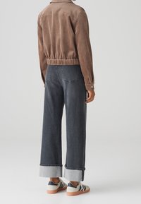 Brown corduroy jacket with elastic waistband, paired with dark gray wide-leg jeans featuring a cuffed hem and beige sneakers.