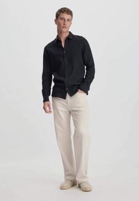 Zwarte linnen blouse met lange mouwen, gecombineerd met crèmekleurige wijde broek en beige espadrilles, wat zorgt voor een ontspannen uitstraling.