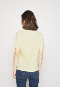 T-shirt giallo chiaro a maniche corte con scollatura rotonda, texture morbida e spacchi laterali, indossato con jeans blu scuro. Vista da dietro.