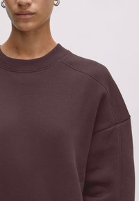 Bordeaux sweatshirt met een ronde halslijn, ribgebreide kraag en raglanmouwen. Gladde textuur, minimalistisch ontwerp en geen zichtbare patronen of accenten.