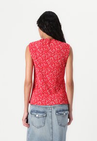 Rød ermeløs topp med plissédesign og små hvite blomsterprint; matchet med lys blå denimskjørt med to baklommer.