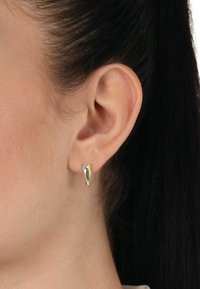 Pendientes de perno en forma de gota de oro y plata, con superficie lisa y acabado pulido, montados en la oreja de un modelo, mostrando un diseño elegante y un contraste de colores.