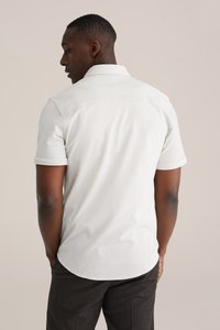 Lichtgrijs poloshirt met een kraag en opgerolde korte mouwen, gemaakt van gladde stof. Opvallende naaddetails aan de achterkant.