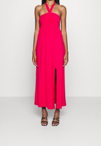 Rosa Halterneck-Kleid mit gerafftem Oberteil und seitlichem Schlitz, kombiniert mit schwarzen Riemchensandalen. Glattes, leichtes Material.