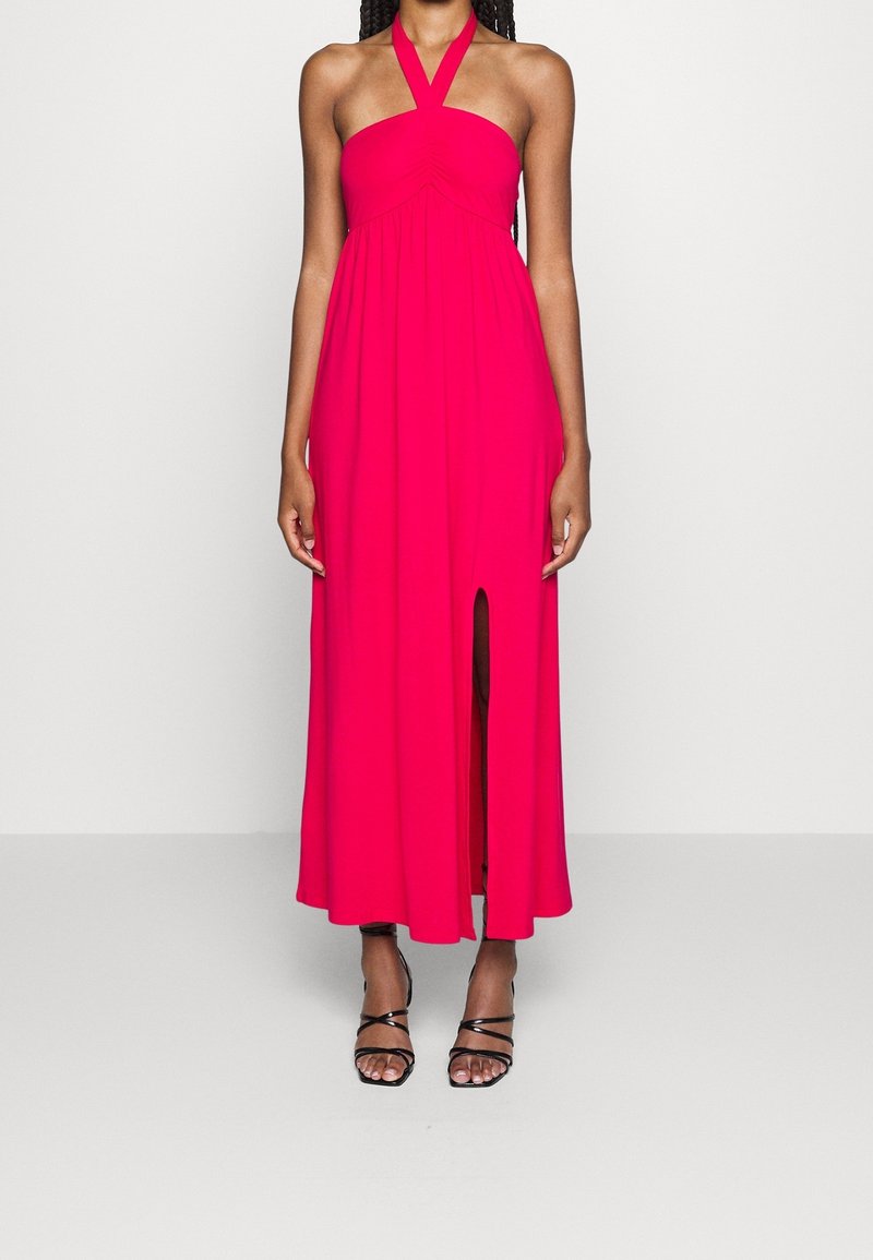 Rosa Halterneck-Kleid mit gerafftem Oberteil und seitlichem Schlitz, kombiniert mit schwarzen Riemchensandalen. Glattes, leichtes Material.