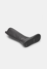 Must musta põlvik, millel on lame kummitald, minimaalne disain, sile tekstuur ja pealmises osas tõmmits mugavaks jalga panemiseks.