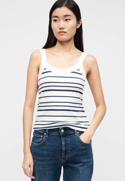 Bijeli top s tankim naramenicama, tamnoplave vodoravne pruge, široke naramenice i okrugli izrez, u paru s tamnoplavim trapericama.