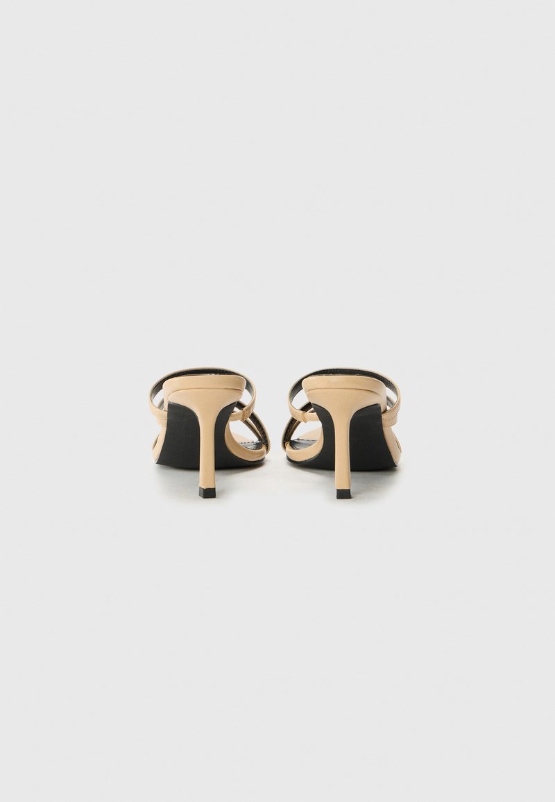 Sandales nude à talons hauts avec des fines brides noires et un design épuré. Présentent un bout pointu et un talon aiguille élancé.