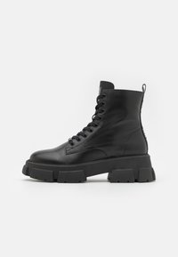 Botas de cuero negro hasta el tobillo con suelas de goma gruesa, puntera redonda y sistema de cordones en la parte frontal. Incluye una lengüeta y detalles texturizados en los costados.