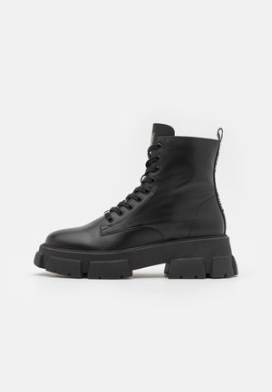 Black leather ankle boots with thick rubber soles, round toe, and lace-up front. Features a pull tab and textured detailing on the sides.