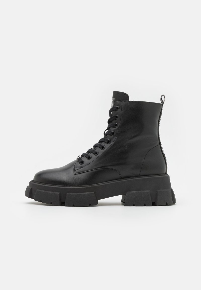 Botas de cuero negro hasta el tobillo con suelas de goma gruesa, puntera redonda y sistema de cordones en la parte frontal. Incluye una lengüeta y detalles texturizados en los costados.
