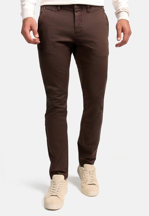 Chinos marrones de corte slim, hechos de una tela suave, con una parte delantera plana y una textura sutil. Combinados con zapatillas color beige claro.