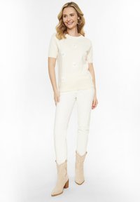 Cremefarvet kortærmet sweater med blomsterbroderi, parret med hvide slim-fit bukser og beige cowboyboots med struktureret overflade.
