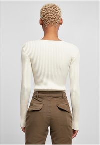 Ribbed, long-sleeve top in off-white, paired with brown pants featuring back pockets. The fit is slim with a rounded neckline.