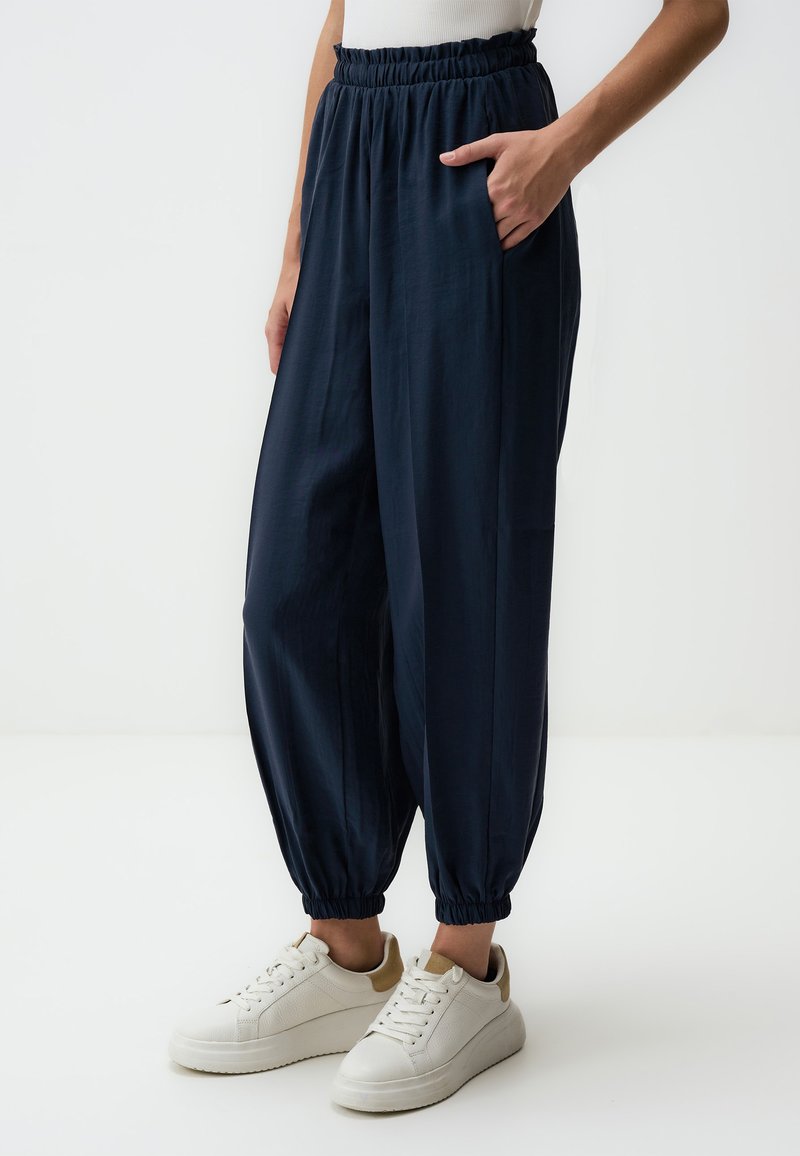 Marineblauwe, lichte tapered broek met een elastische tailleband en cuffs bij de enkels, met zijzakken. Draag met witte sneakers.