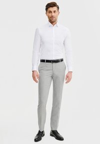 Biała koszula z długim rękawem o dopasowanym kroju, zestawiona z jasnoszarymi spodniami wizytowymi, czarnym skórzanym paskiem i czarnymi butami, stojąca na neutralnym tle.