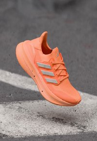 Φωτεινό πορτοκαλί αθλητικό παπούτσι με υφασμάτινο επάνω μέρος με υφή, τρεις ασημένιες ρίγες και μαλακό πέλμα. Ελαφρύ σχέδιο για τρέξιμο.