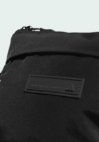 Borsa in tessuto nero con superficie strutturata, dotata di chiusura con cerniera e un'etichetta rettangolare nera con testo in rilievo e logo.