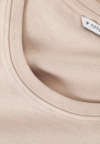 T-shirt en coton beige avec un col rond, présentant une texture douce et un détail de couture subtil le long du col. Étiquette de marque visible.