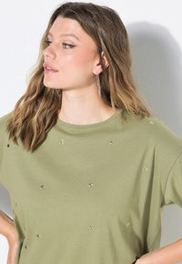 Oliwkowa koszulka z krótkim rękawem, ozdobiona metalicznymi gwiazdkami i okrągłym dekoltem, wykonana z miękkiego, elastycznego materiału.