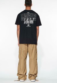 Black cotton t-shirt with bold white text on the back. Paired with beige cargo pants featuring multiple pockets and a relaxed fit.