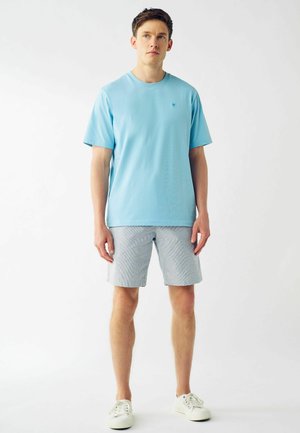 Tricou din bumbac de culoare albastru deschis, cu mâneci scurte, asortat cu pantaloni scurți gri cu dungi și adidași albi. Design simplu, fără logo-uri vizibile.