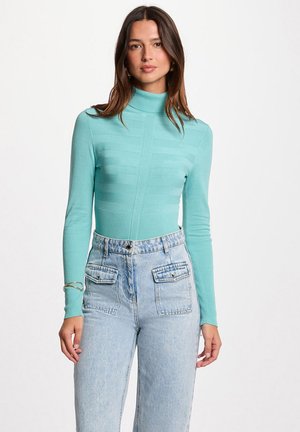 Maglione aderente turchese a collo alto con texture a costine e pannelli orizzontali, abbinato a jeans in denim azzurro chiaro a vita alta con tasche.