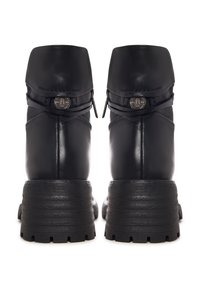 Paire de bottines noires en cuir avec semelles en caoutchouc épaisses, brides arrière et ornements métalliques circulaires avec logo.
