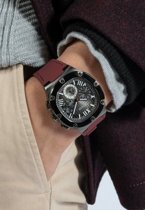 Montre noire et argent avec un cadran noir texturé, des index horaires blancs et des sous-dials. Elle est dotée d'un bracelet en caoutchouc bordeaux et d'accents métalliques.