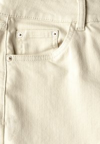Jean en denim beige avec une petite poche avant, des rivets en métal argenté et une finition lisse. Coutures le long des bords.