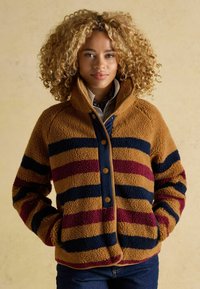 Bikseņu jaka gaišbrūnā tonī ar bordo un tumši zilu svītru, ar augstu apkakli, pogu aizdari un priekšējiem kabatām. Mīksts, teksturēts audums.