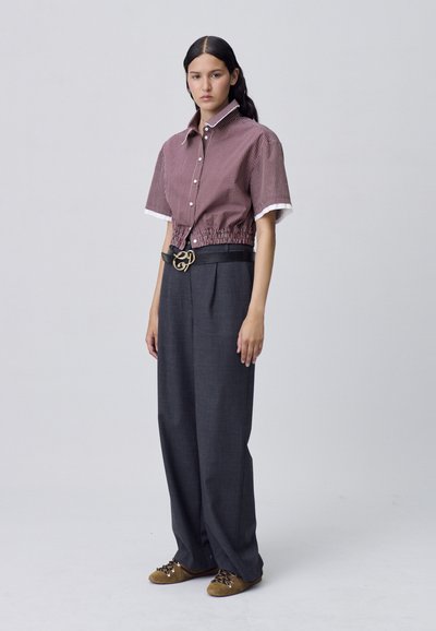 Camisa corta de cuadros rojos y blancos con mangas cortas y cintura ajustada. Pantalones oscuros de talle alto gris oscuro, cinturón negro con detalles dorados, zapatos marrones.