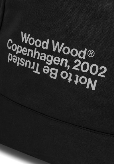 Fekete szövet, amelyen fehér felirat olvasható: "Wood Wood® Copenhagen, 2002 Nem megbízható" átlós elrendezésben.