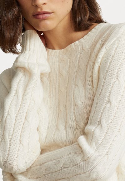 Pull crème en tricot torsadé avec un col rond et des poignets côtelés, fabriqué à partir d'un tissu doux et texturé, offrant une coupe confortable et décontractée.