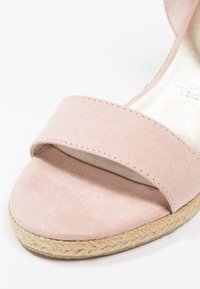 Gros plan d'une sandale en daim rose clair avec une large lanière avant et une semelle espadrille en jute tressée.
