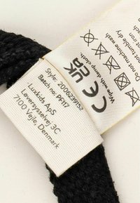 Black textile label featuring washing symbols, brand name "Luxkids APS," style number, and care instructions, attached to a black garment.